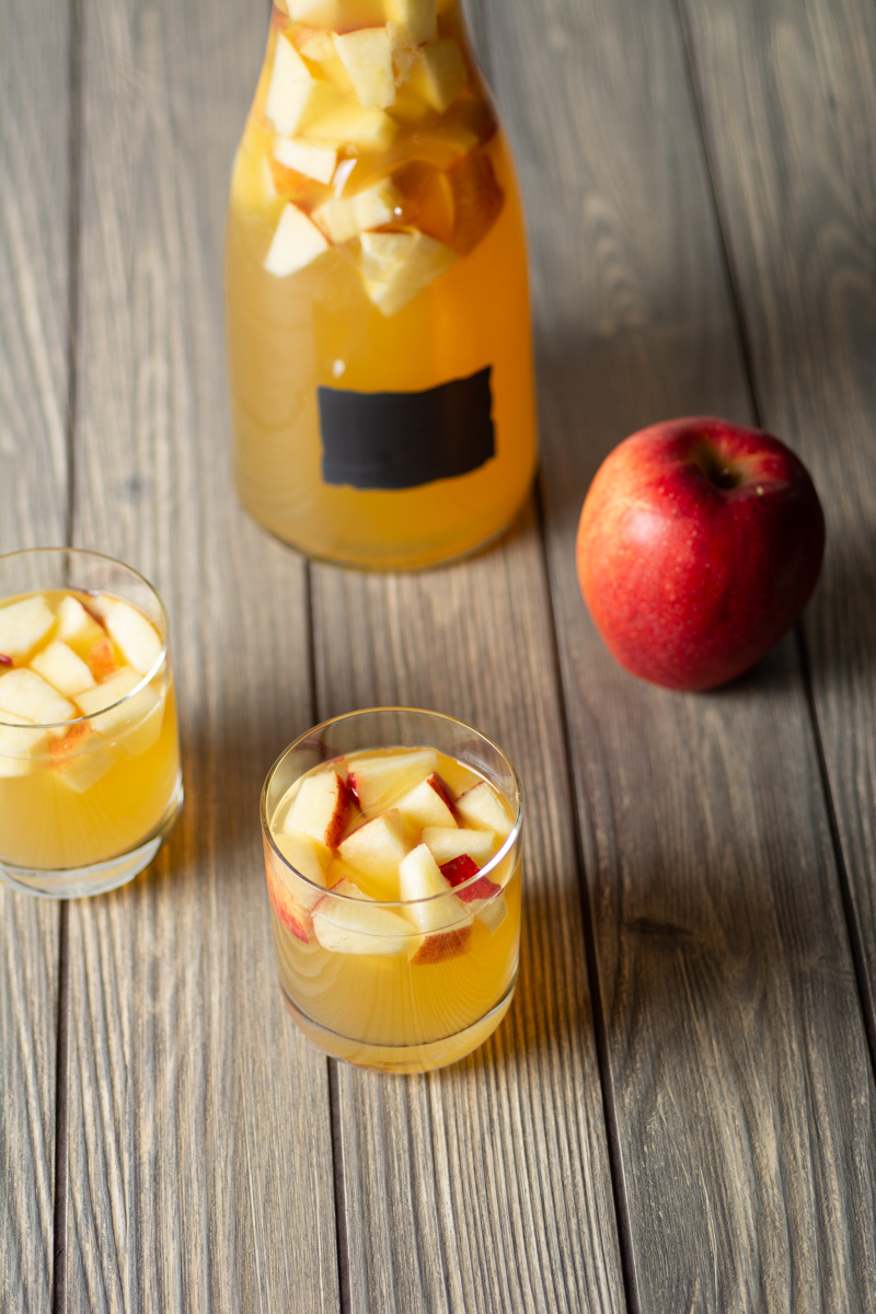 Caramel apple sangria in glasses with carafe and apple in background.