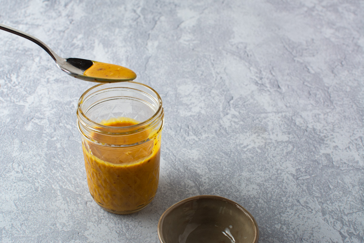 A spoon full of hot honey mustard sauce and a glass mason jar.