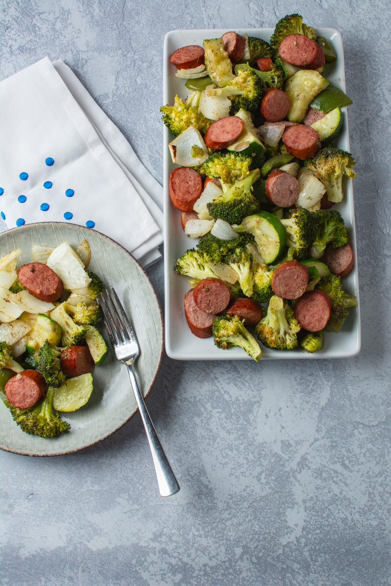 Sheet pan turkey sausage and vegetables cooked and on a serving plate and small dinner plate.
