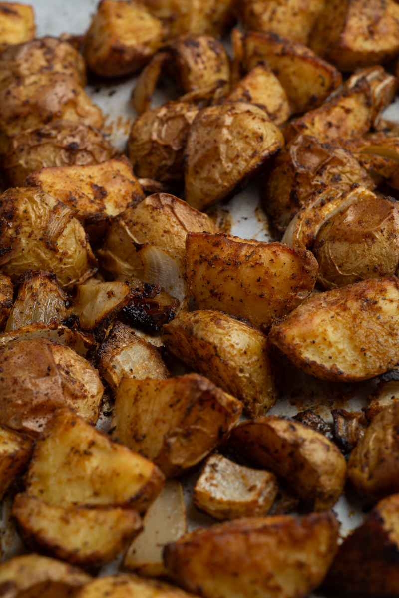 Close-up of roasted potatoes with onions on a sheet pan with parchment paper.